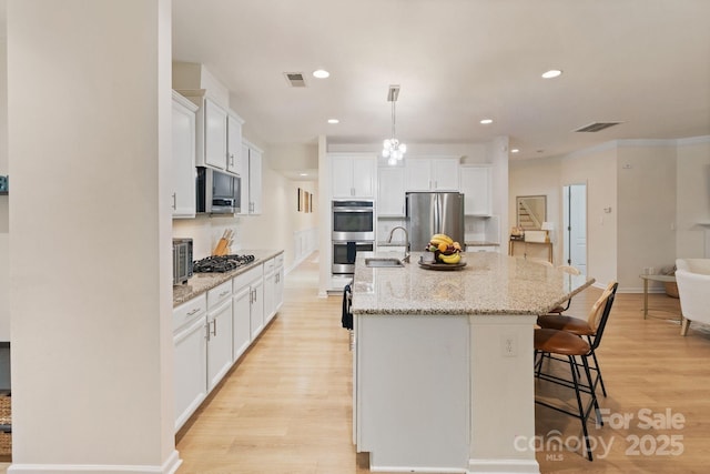1104 Snowbird Ln, Waxhaw, NC 28173 - kitchen with stainless steel appliances, a breakfast bar area, a sink, light wood-type flooring, and white cabinetry