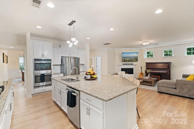 1104 Snowbird Ln, Waxhaw, NC 28173 - kitchen featuring stainless steel appliances, a lit fireplace, a sink, a center island with sink, and white cabinets