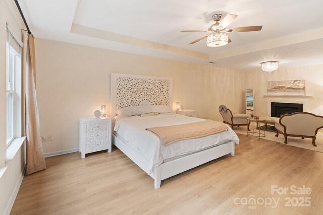 1104 Snowbird Ln, Waxhaw, NC 28173 - bedroom with a tray ceiling, light wood-type flooring, a fireplace, and baseboards