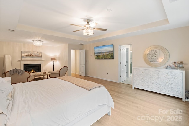 1104 Snowbird Ln, Waxhaw, NC 28173 - bedroom featuring a tray ceiling, light wood finished floors, baseboards, and a warm lit fireplace