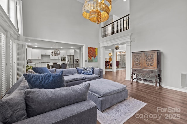 9625 Donna Ve Ln, Charlotte, NC 28277 - living area featuring ornate columns, a chandelier, dark wood finished floors, a high ceiling, and baseboards
