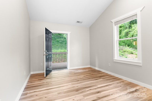 empty room with plenty of natural light, light wood finished floors, vaulted ceiling, and baseboards