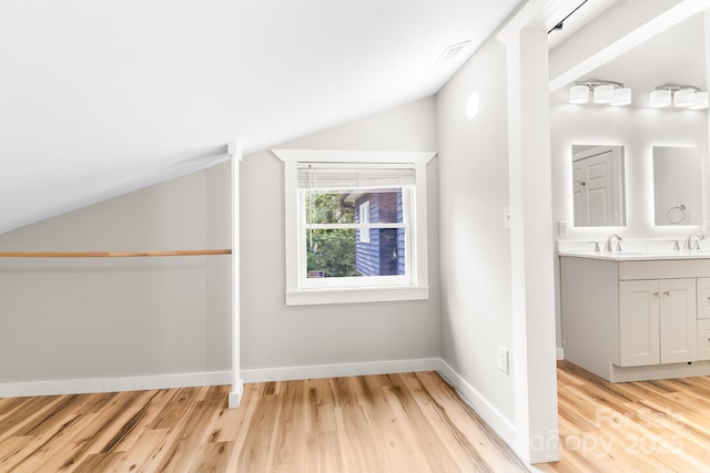 additional living space featuring lofted ceiling, light wood-type flooring, baseboards, and a sink