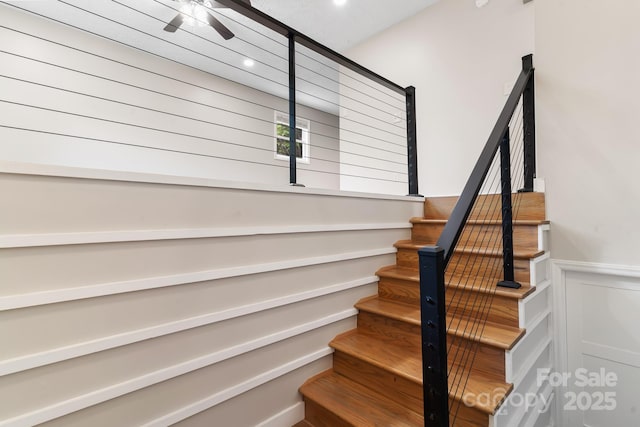 stairs with wainscoting, recessed lighting, ceiling fan, and a decorative wall