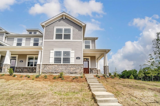 view of front of house featuring covered porch, stone siding, and a front lawn