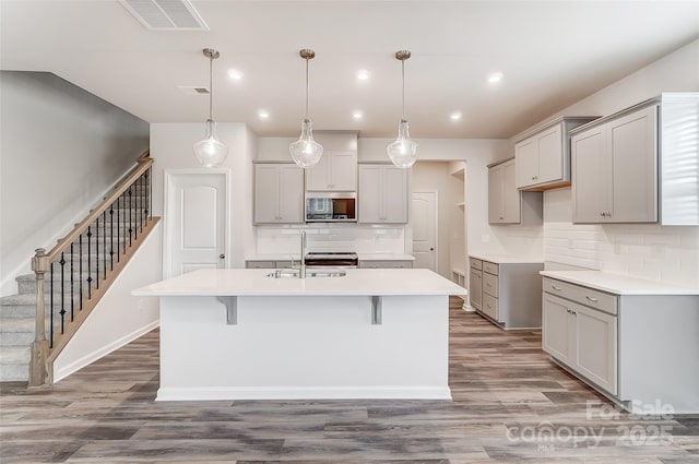 kitchen featuring a sink, gray cabinets, a kitchen island with sink, and recessed lighting