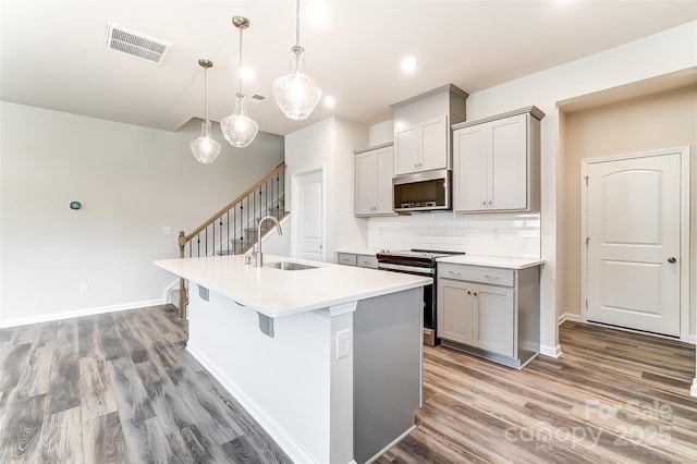 kitchen with appliances with stainless steel finishes, a sink, gray cabinetry, light wood-style flooring, and a kitchen island with sink