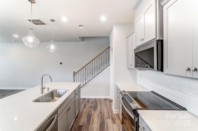 kitchen with stainless steel appliances, a sink, decorative light fixtures, dark wood finished floors, and baseboards