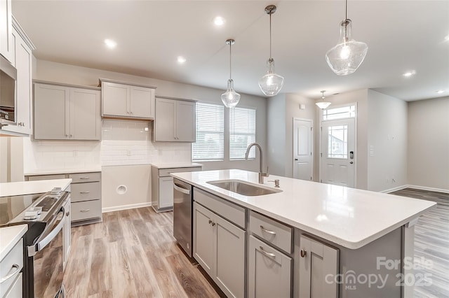 kitchen featuring a sink, gray cabinetry, appliances with stainless steel finishes, backsplash, and light wood finished floors