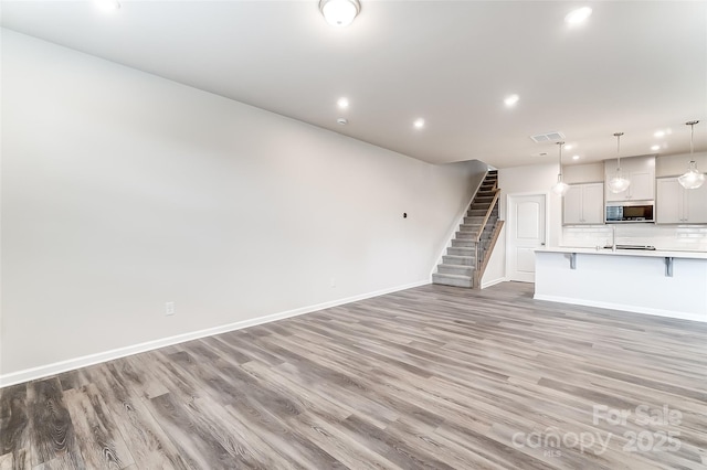 unfurnished living room with light wood-style flooring, stairs, recessed lighting, and baseboards