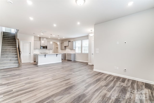 unfurnished living room featuring light wood-style floors, baseboards, stairway, and recessed lighting