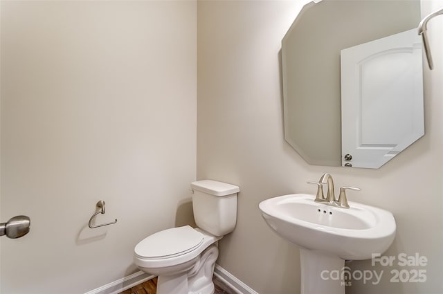 half bathroom featuring a sink, toilet, baseboards, and wood finished floors