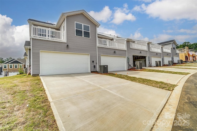 back of property with an attached garage, driveway, a balcony, and central AC unit