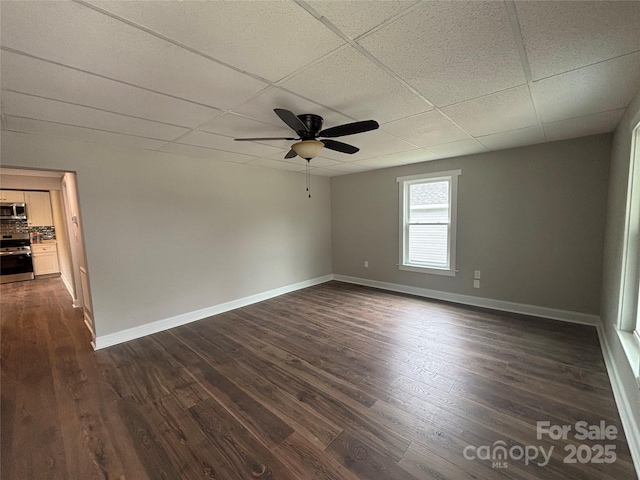 empty room with ceiling fan, baseboards, dark wood-type flooring, and a paneled ceiling