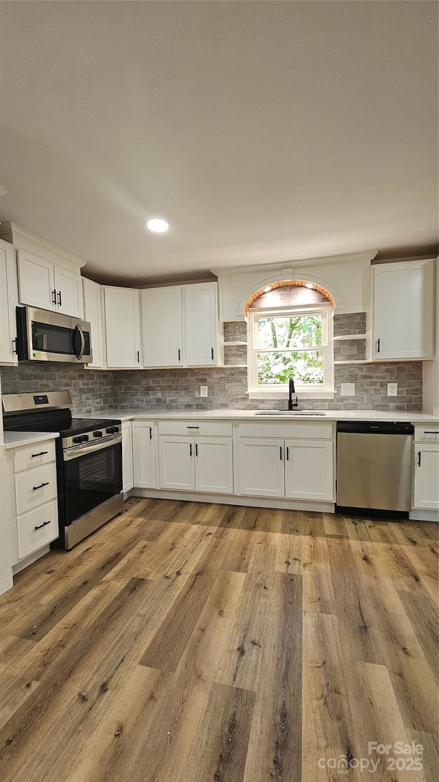 7021 Linda Lake Dr, Charlotte, NC 28215 - kitchen with stainless steel appliances, a sink, open shelves, tasteful backsplash, and light wood-style floors