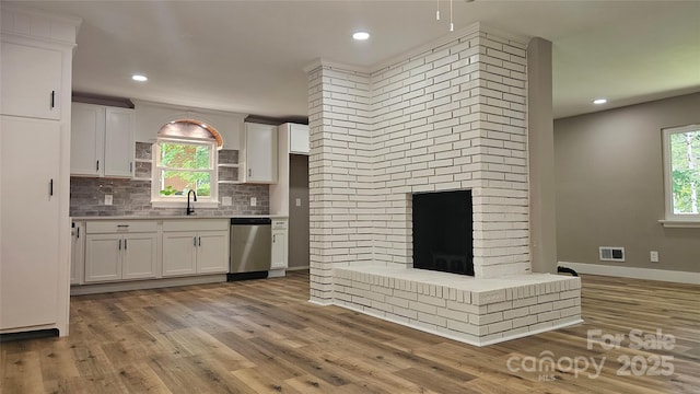 7021 Linda Lake Dr, Charlotte, NC 28215 - kitchen featuring stainless steel dishwasher, white cabinetry, a sink, light wood-style floors, and backsplash