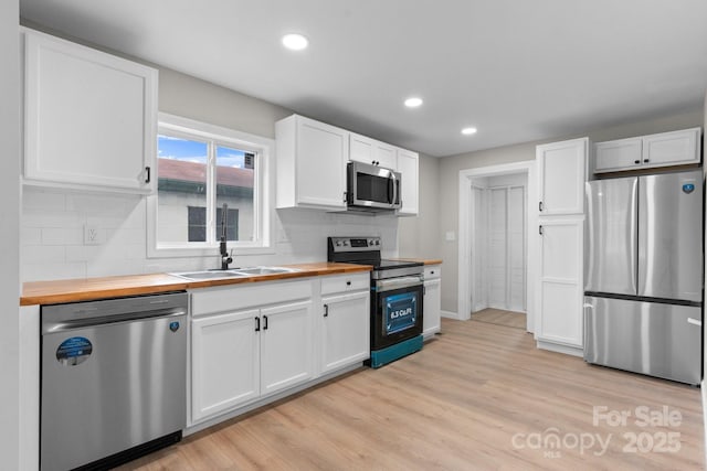 kitchen with stainless steel appliances, wooden counters, white cabinets, a sink, and backsplash