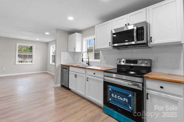 kitchen featuring stainless steel appliances, butcher block countertops, a sink, tasteful backsplash, and light wood finished floors