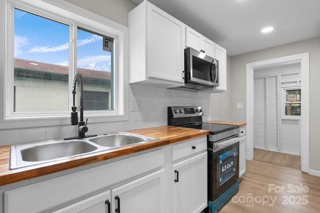 kitchen featuring appliances with stainless steel finishes, butcher block counters, a sink, white cabinets, and decorative backsplash