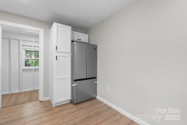 kitchen featuring freestanding refrigerator, white cabinetry, light wood-style floors, and baseboards