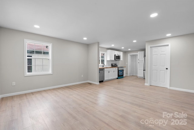 unfurnished living room featuring recessed lighting, baseboards, light wood finished floors, and a sink