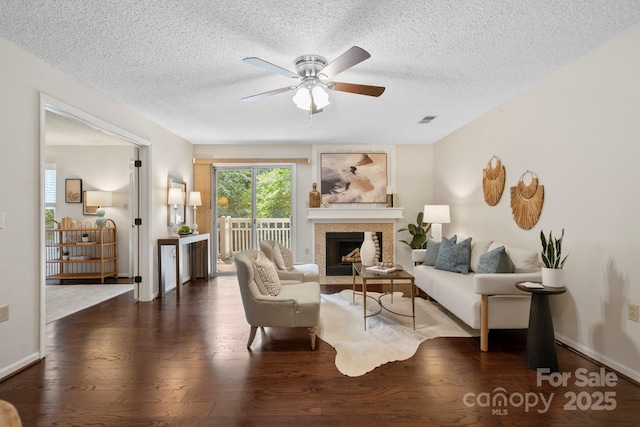 living area with wood-type flooring, ceiling fan, a fireplace with flush hearth, and a textured ceiling
