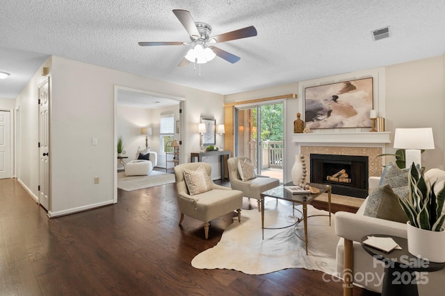 living room with wood finished floors, a ceiling fan, a fireplace, a textured ceiling, and baseboards
