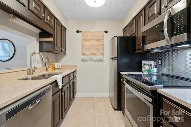 kitchen featuring stainless steel appliances, a sink, dark brown cabinetry, decorative backsplash, and baseboards