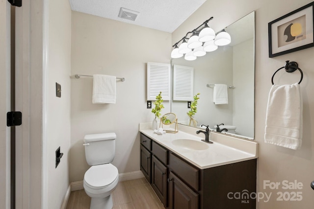bathroom featuring toilet, vanity, baseboards, a textured ceiling, and wood finished floors