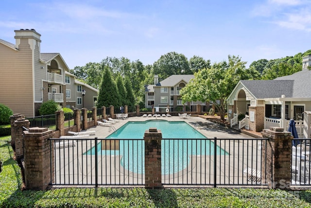 community pool with a patio, fence, and a residential view