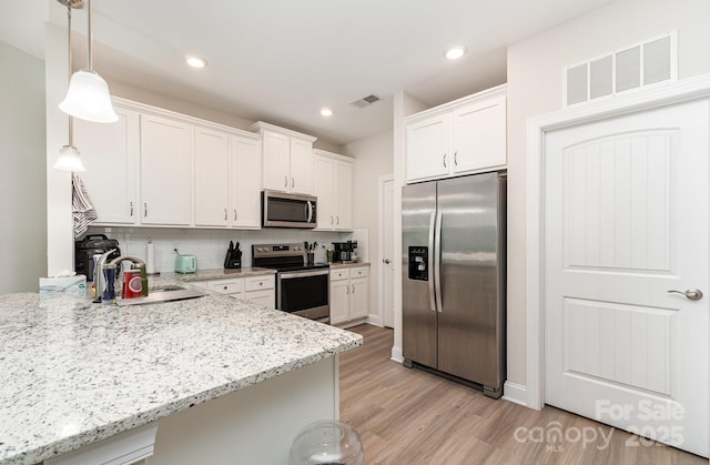 kitchen featuring appliances with stainless steel finishes, a sink, white cabinets, light wood-type flooring, and recessed lighting