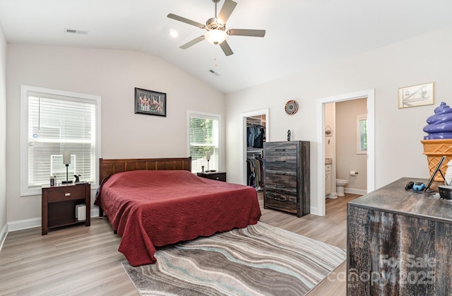 bedroom featuring lofted ceiling, a walk in closet, light wood-type flooring, a closet, and ensuite bath