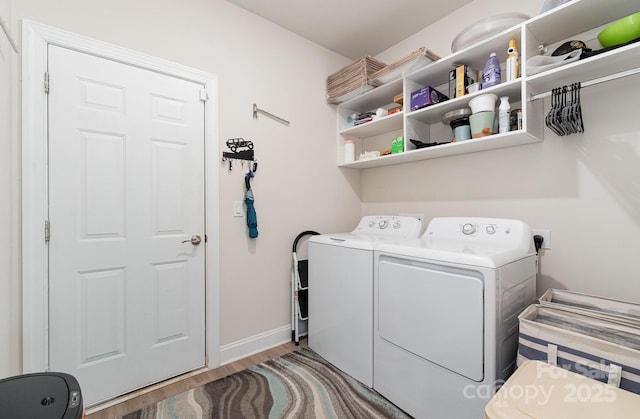 clothes washing area with washing machine and clothes dryer, wood finished floors, and baseboards