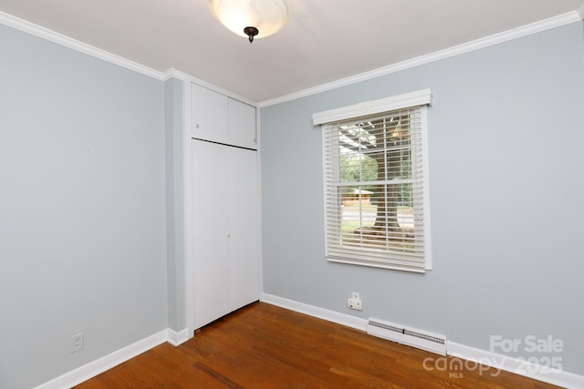 unfurnished bedroom featuring a baseboard heating unit, a closet, crown molding, dark wood-style floors, and baseboards