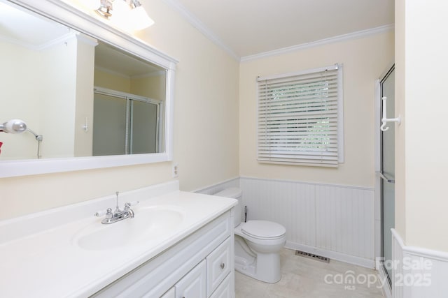 bathroom featuring a stall shower, wainscoting, vanity, crown molding, and toilet