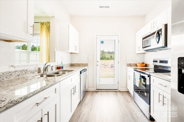 kitchen with appliances with stainless steel finishes, a sink, light wood-style flooring, white cabinetry, and light stone countertops