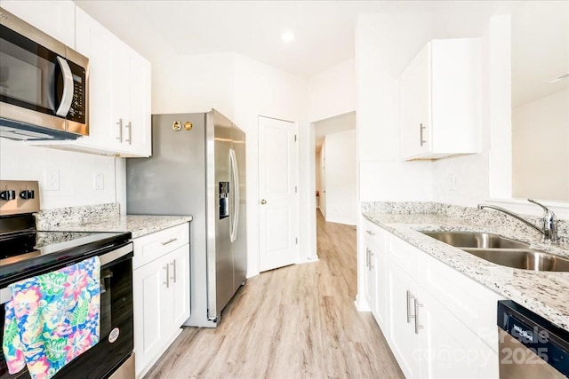 kitchen with stainless steel appliances, a sink, light wood-style floors, and white cabinetry