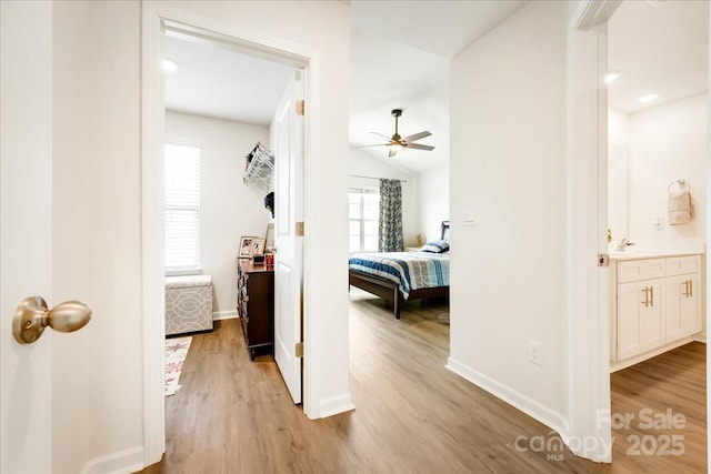 corridor with light wood-style floors, baseboards, vaulted ceiling, and a sink