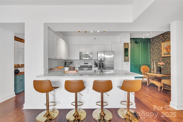 kitchen featuring stainless steel appliances, track lighting, a peninsula, dark wood-style floors, and white cabinets