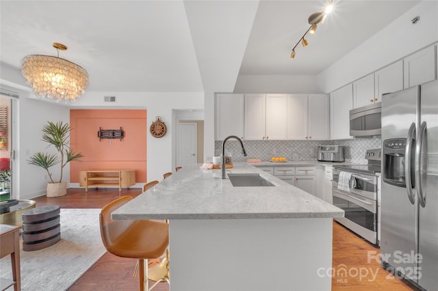 kitchen featuring stainless steel appliances, a sink, tasteful backsplash, light stone countertops, and rail lighting