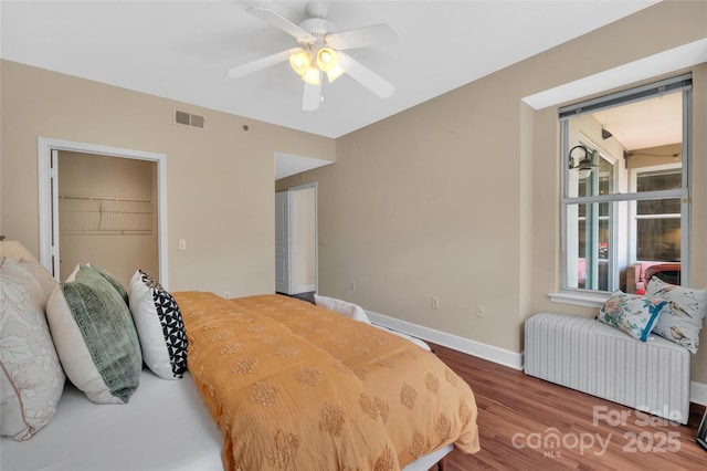 bedroom with wood finished floors, baseboards, a closet, a walk in closet, and ceiling fan