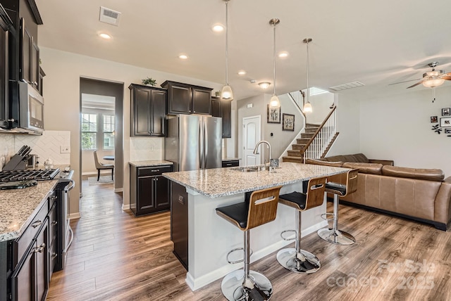 kitchen featuring stainless steel appliances, a sink, open floor plan, a kitchen breakfast bar, and a ceiling fan