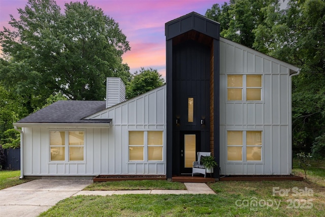 6824 Cortez Trl, Charlotte, NC 28227 - back of property at dusk with board and batten siding, a chimney, a shingled roof, and a lawn