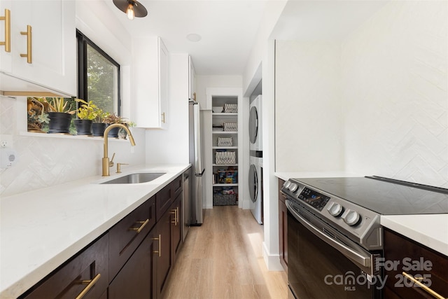 6824 Cortez Trl, Charlotte, NC 28227 - kitchen with appliances with stainless steel finishes, estacked washer and dryer, a sink, light wood-style flooring, and white cabinets
