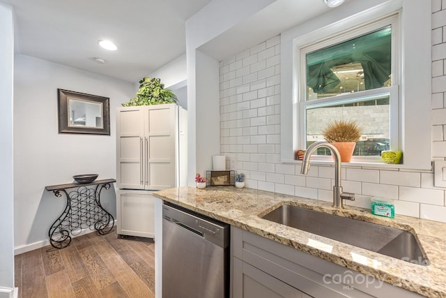 kitchen featuring stainless steel dishwasher, a sink, wood finished floors, and tasteful backsplash