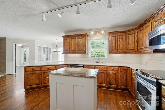 1295 Patterson St, China Grove, NC 28023 - kitchen featuring stainless steel appliances, a peninsula, a sink, brown cabinets, and rail lighting