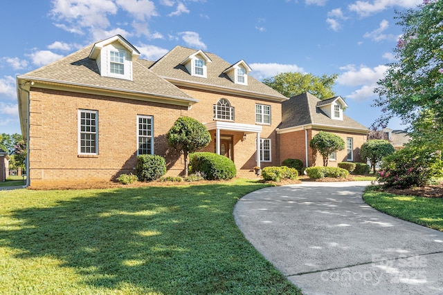 colonial home featuring brick siding, a front lawn, a shingled roof, and curved driveway