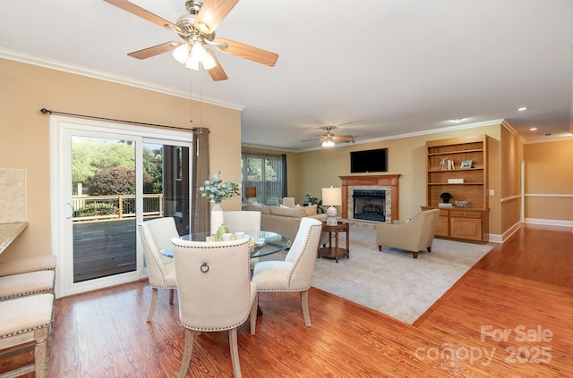 dining area with ceiling fan, light wood-type flooring, a fireplace with raised hearth, ornamental molding, and recessed lighting