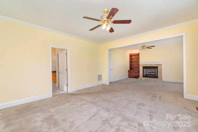 unfurnished living room featuring ornamental molding, carpet floors, ceiling fan, a fireplace with raised hearth, and baseboards