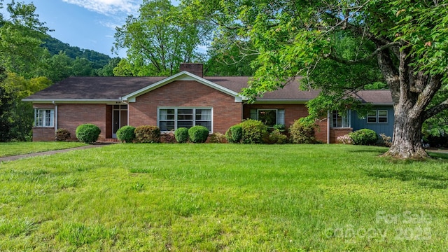 ranch-style home featuring a chimney, brick siding, and a front yard